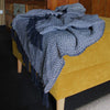 A navy and white cotton throw blanket with a herringbone zigzag pattern and dark blue fringe for cozy comfort