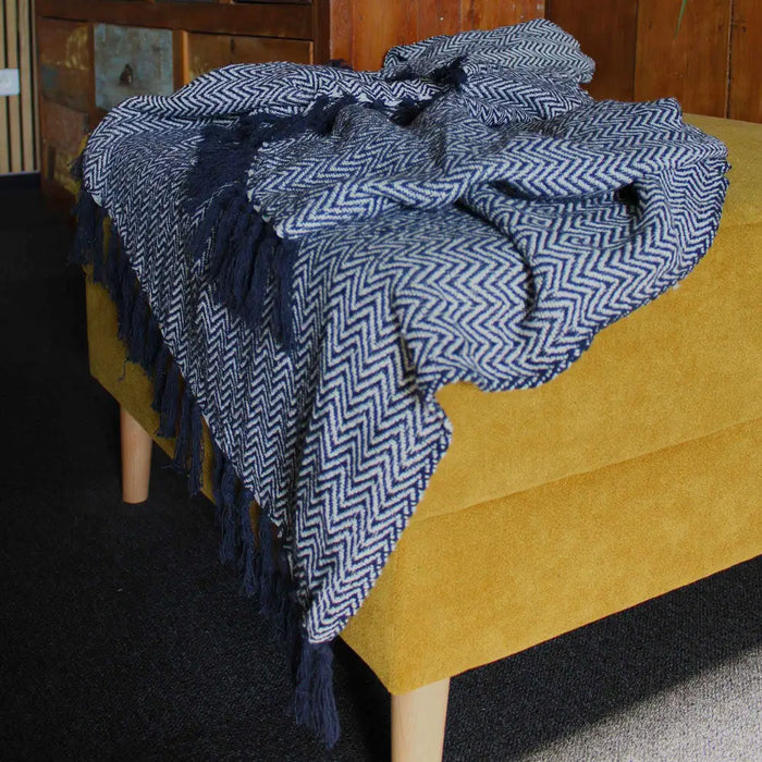 A navy and white cotton throw blanket with a herringbone zigzag pattern and dark blue fringe for cozy comfort