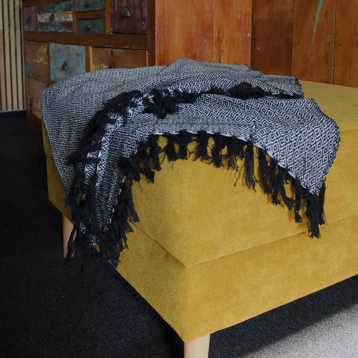 Black and white geometric cotton comfort throw with fringed edges draped over mustard yellow ottoman versatile piece