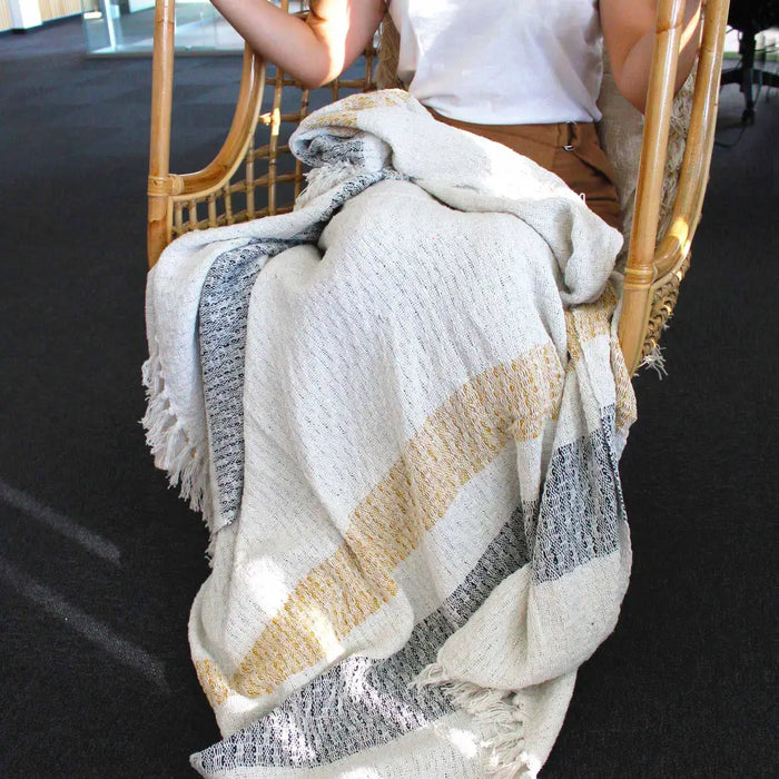 A cozy cotton throw blanket with wide diagonal stripes in cream mustard yellow and gray featuring fringed edges