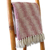 A cozy cotton throw blanket in ruby and cream with a woven texture and soft tassels along the edge