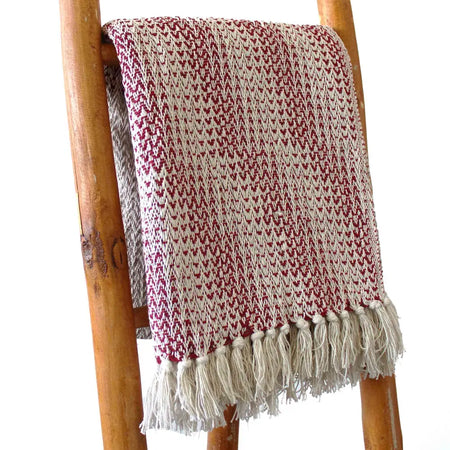 A cozy cotton throw blanket in ruby and cream with a woven texture and soft tassels along the edge