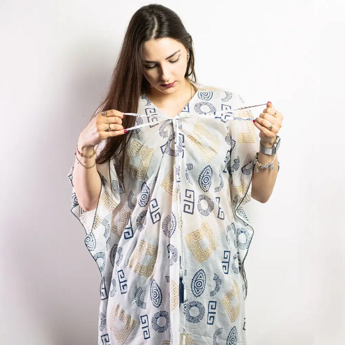 A flowing white cotton kaftan with navy blue and gold geometric and circular motifs inspired by greek design