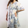 A white cotton kaftan dress with blue and gold geometric patterns flowing on a plain background