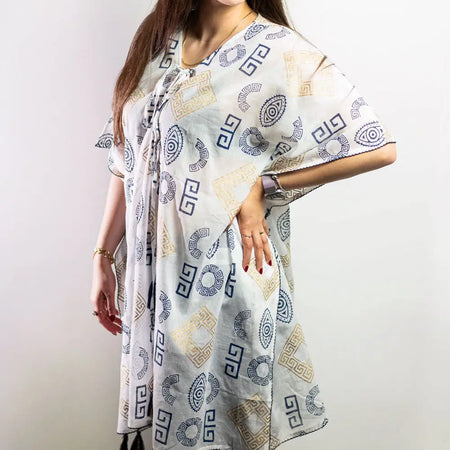 A white cotton kaftan dress with blue and gold geometric patterns flowing on a plain background