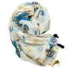 A delicate off-white cotton pareo with blue and gold evil eye sunburst patterns and black tassels at the ends
