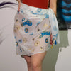A sheer white cotton pareo wrap skirt with blue and gold evil eye motifs and a decorative tassel at the side
