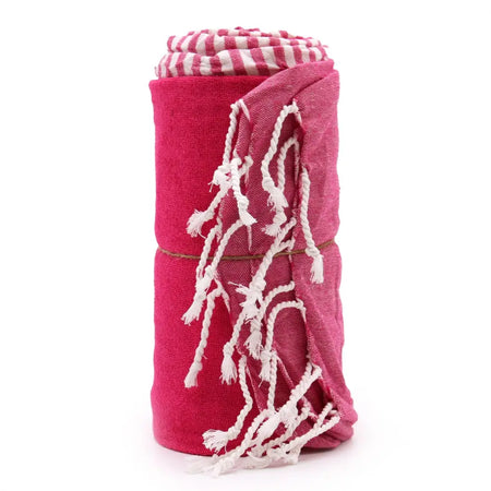 A rolled-up cotton pario towel in hot pink with white stripes and fringed edges