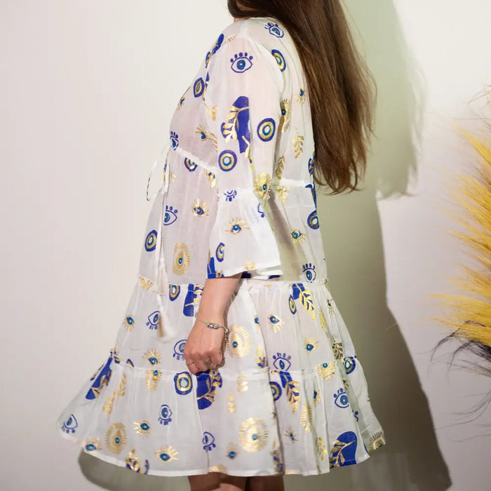 A white cotton print dress with blue and gold evil eye motifs and a semi sheer tiered nomad sari style design