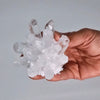 A hand holds a clear quartz cluster with sharp pointed translucent faceted crystals made of clear quartz