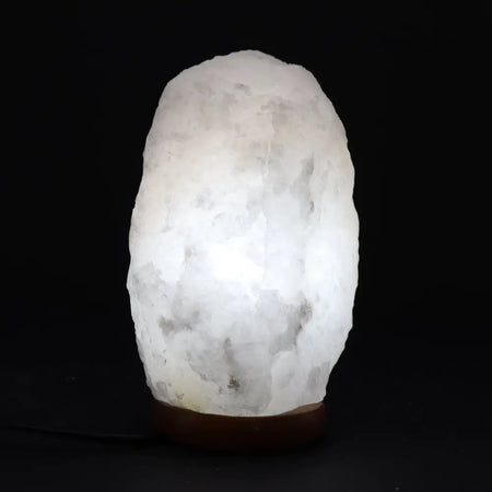 A glowing white crystal rock himalayan salt lamp with rough texture and gray veins showing its hygroscopic properties
