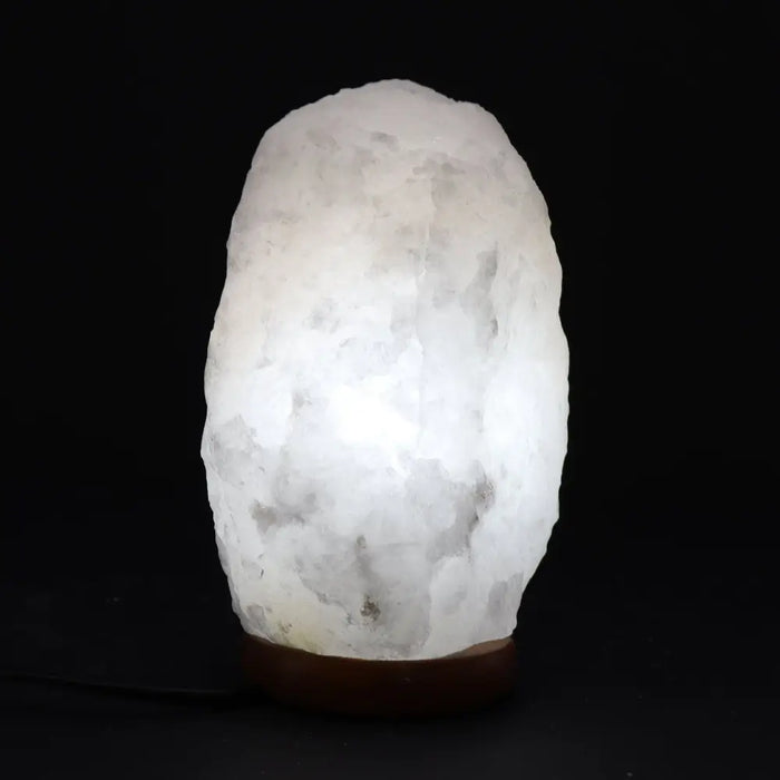 A glowing white crystal rock himalayan salt lamp with rough texture and gray veins showing its hygroscopic properties