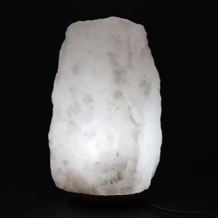 A glowing white crystal rock himalayan salt lamp with rough texture and subtle gray veining showing hygroscopic properties