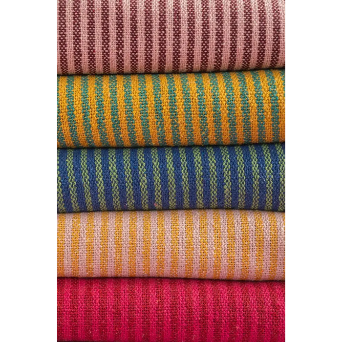 Stack of red and pink striped throw bolts made from recycled cotton fabric in colorful woven patterns