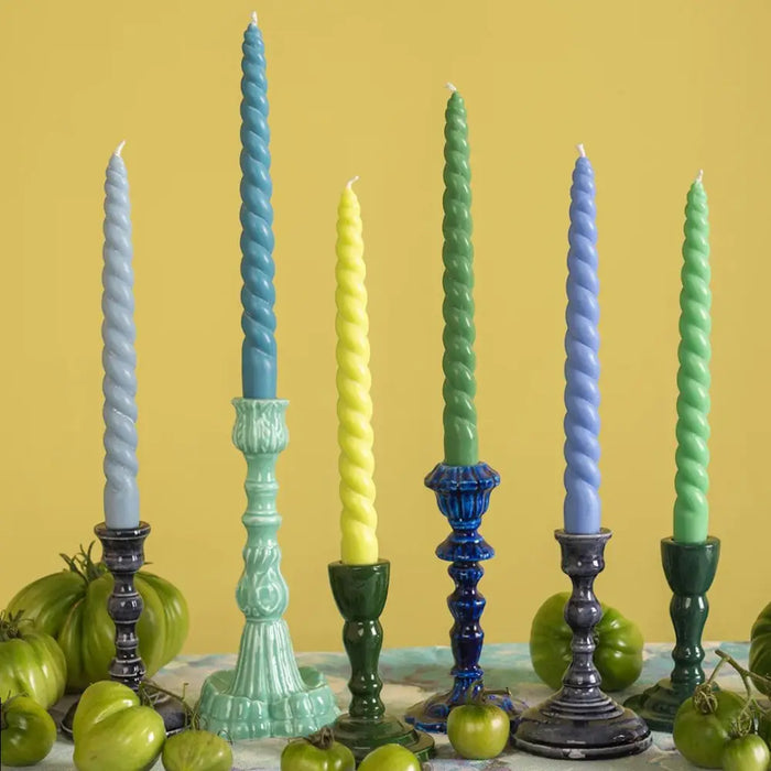 A set of six twisted dinner candles in pastel blue green and yellow on glossy ceramic candlesticks from daisy snow coast