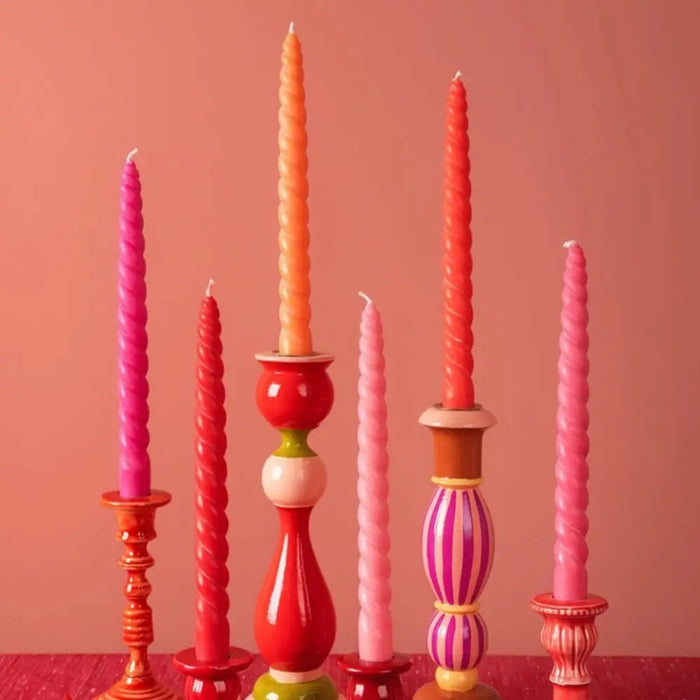 A set of six twisted dinner candles in pink red and orange made with coconut oil by daisy snow on patterned ceramic holders
