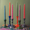A set of six twisted dinner candles in blue orange pink green purple and red on matching ceramic holders