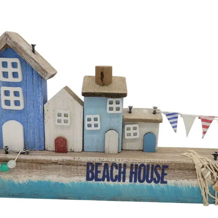 A rustic wooden beach house ornament with painted blue and white houses and nautical rope accents on a wooden base