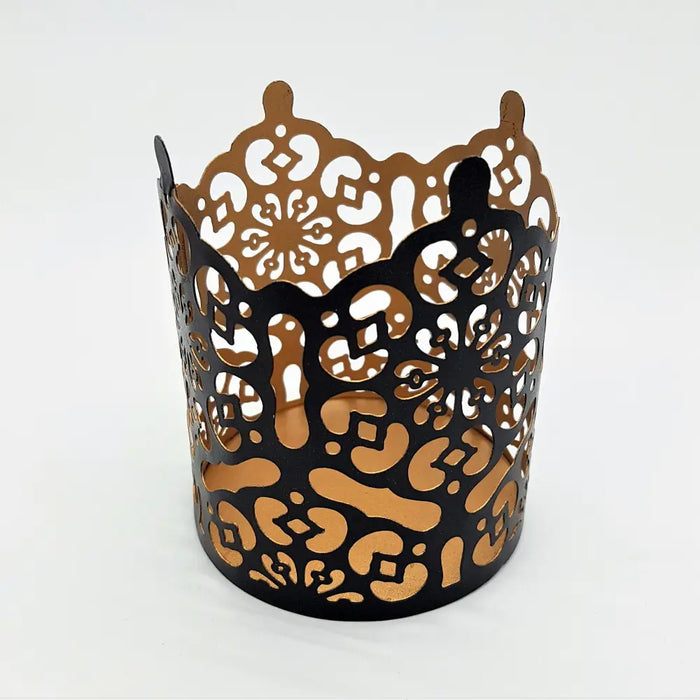 Black and gold die-cut metal votive with intricate floral patterns in a prussian style design
