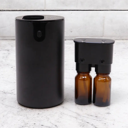 Black cylindrical essential oil waterless nebulizer with two amber glass bottles and a red charging light on usb c base
