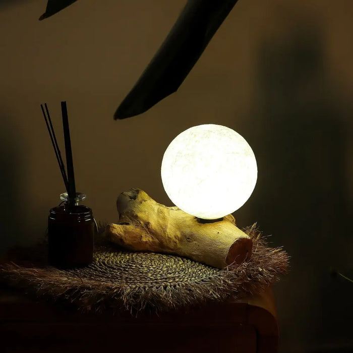 A driftglow lamp with a glowing white cotton wrap shade resting on textured driftwood