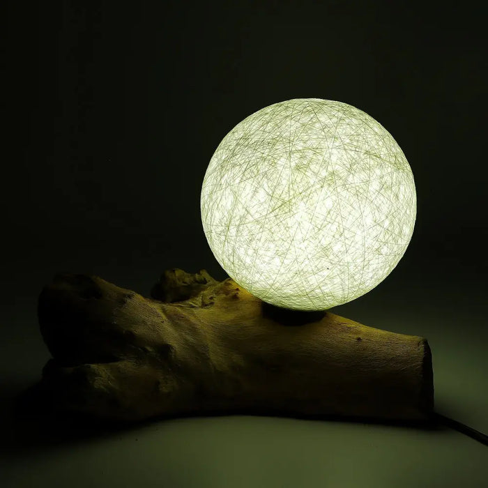 A driftglow lamp featuring a glowing spherical cotton wrap shade with a light green filament on a rustic wooden base