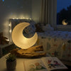 A warm glowing grey fibreglass half-moon shade lamp with a smooth surface on a rustic wooden base