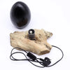 A driftglow lamp with a sleek black oval stone on light driftwood base and grey crackle lava egg shade