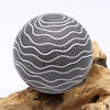 A driftglow lamp with a spherical black crackled surface and silver wavy lines featuring a grey luna shade