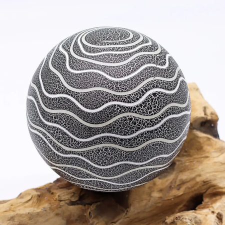 A driftglow lamp with a spherical black crackled surface and silver wavy lines featuring a grey luna shade