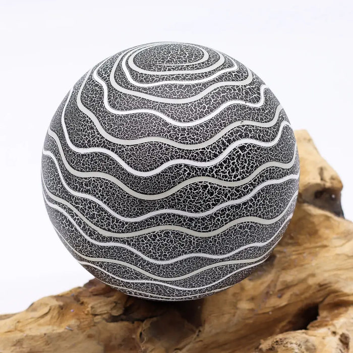 A driftglow lamp with a spherical black crackled surface and silver wavy lines featuring a grey luna shade
