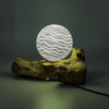 A glowing driftglow lamp with grey luna shade features white wavy patterns on a translucent globe with a wooden base
