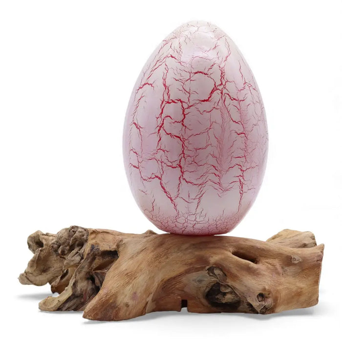 A translucent pink driftglow lamp with red crackle patterns on a rustic wooden base resembling a fire egg shade