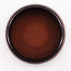 A dark brown clay om buddha earth powder singing bowl with a circular shape and carved floral patterns
