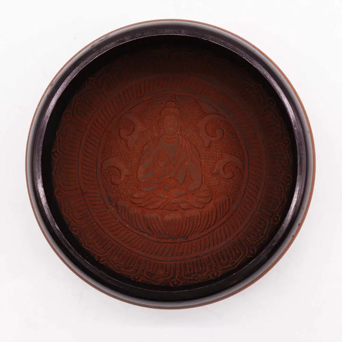 A dark brown clay om buddha earth powder singing bowl with a circular shape and carved floral patterns