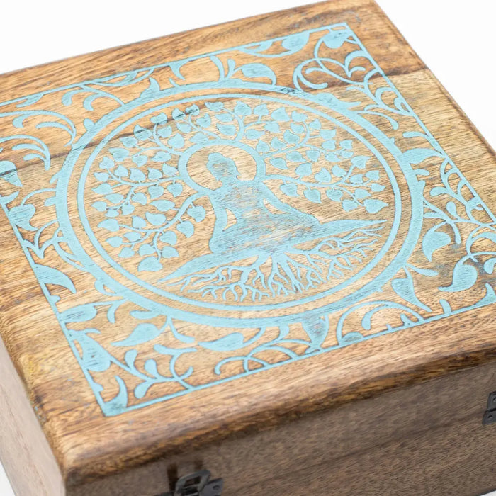 A square mango wood box with a carved turquoise tree of life and a meditating figure at the center