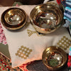 Three polished brass singing bowls of varying sizes on a patterned textile, made of bell-metal and handmade