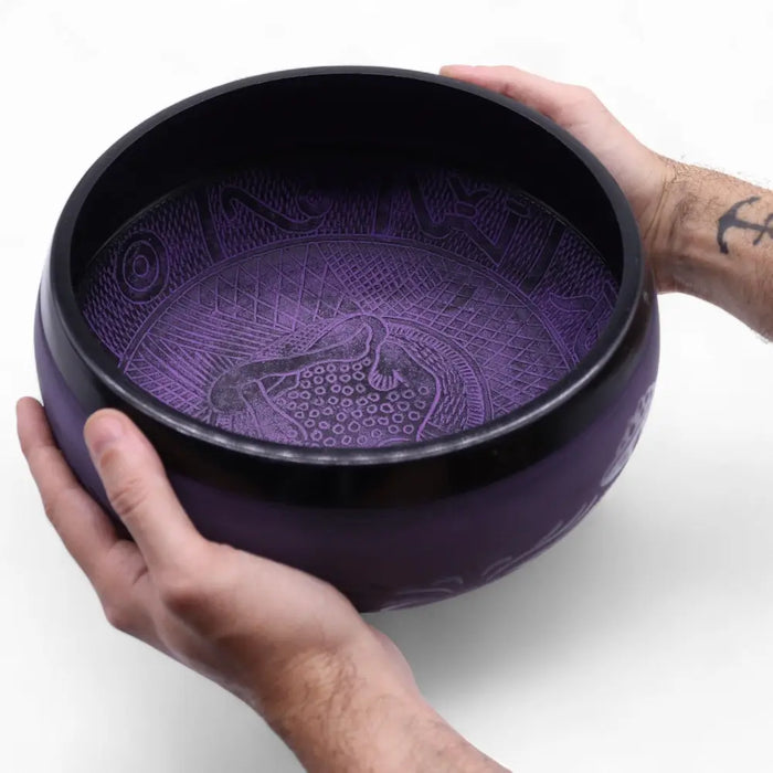 A 5cm high purple haze mushroom singing bowl with intricate engravings and a black rim held in two hands