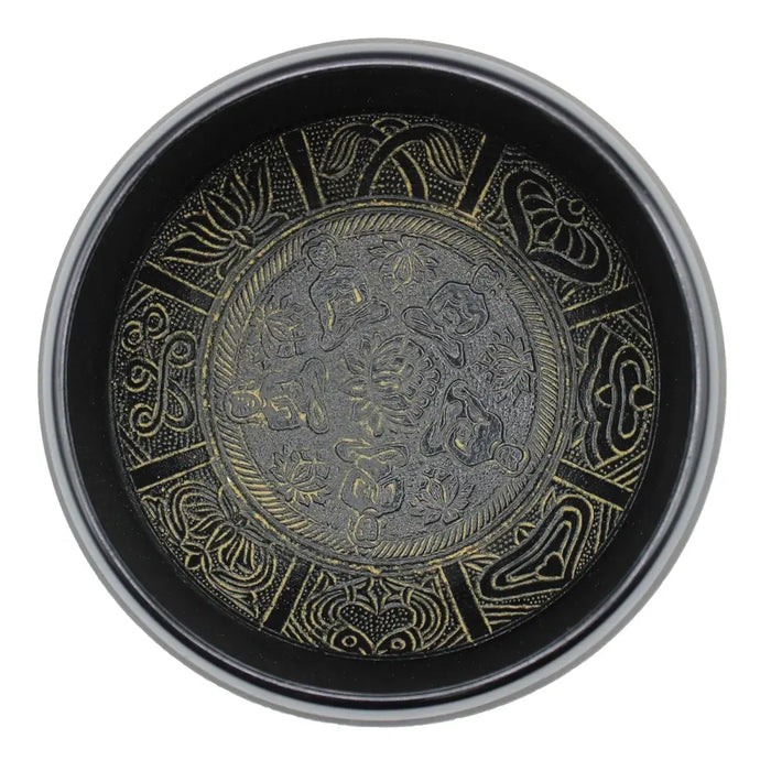 Black circular singing bowl with intricate gold embossed floral and five buddha patterns on metal tray