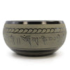 A matte-finished tibetan singing bowl with a polished metallic rim engraved with sanskrit mantras and wave patterns