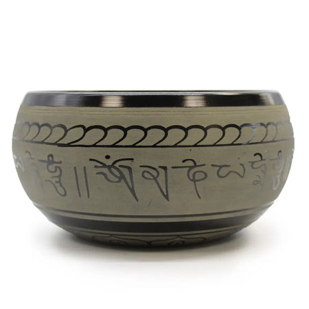 A matte-finished tibetan singing bowl with a polished metallic rim engraved with sanskrit mantras and wave patterns