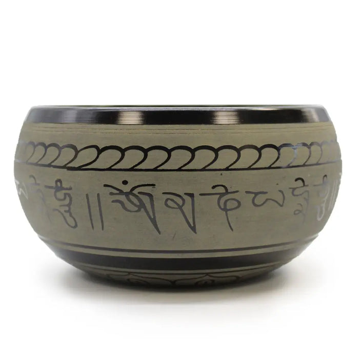 A matte-finished tibetan singing bowl with a polished metallic rim engraved with sanskrit mantras and wave patterns