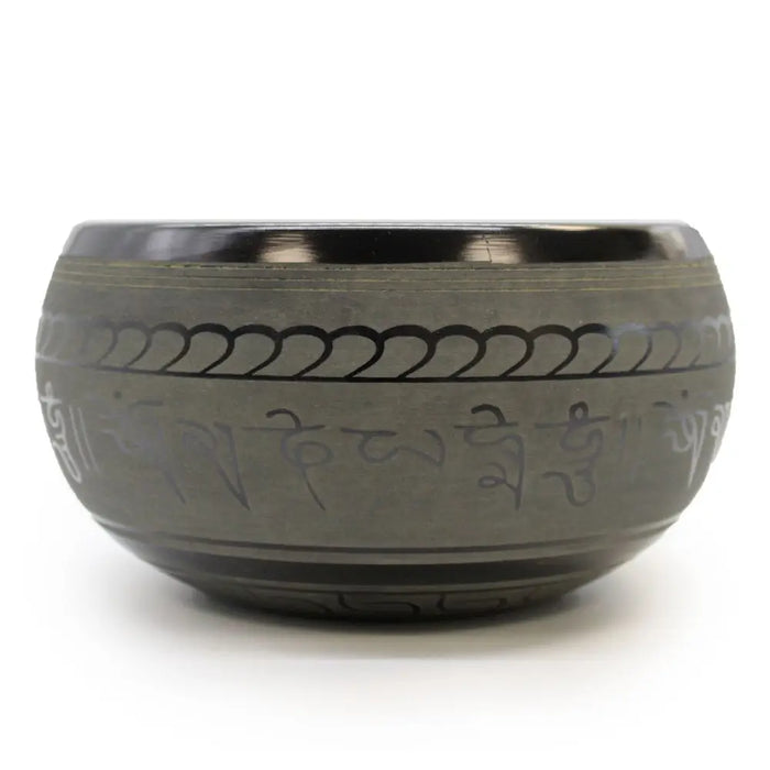 A dark gray extra loud tibetan singing bowl with engraved sanskrit script and decorative patterns made of metal