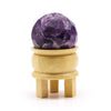 A faceted purple amethyst gemstone healing ball displayed on a light yellow wooden stand for gemstone healing