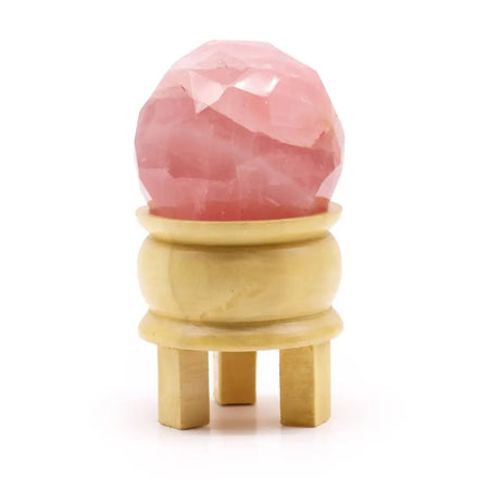Faceted gemstone healing ball made of pink rose quartz displayed on a golden wooden stand