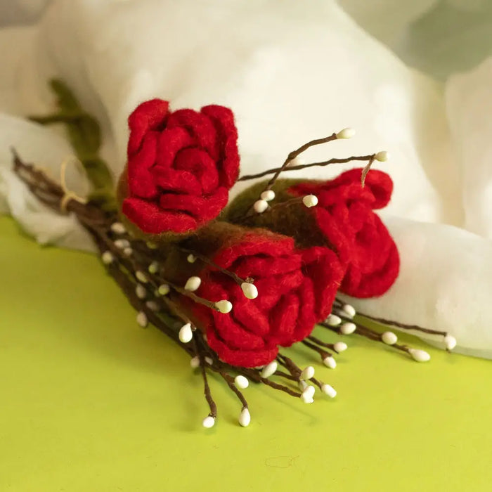 Handcrafted felt flowers showing three red roses with brown stems and small white buds in a simple arrangement