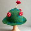 A whimsical moss mountain green felted mushroom hat with red and white spotted felt mushrooms and textured surface
