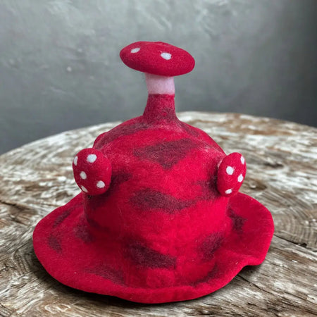 A red felted mushroom hat with white polka dots and side knobs made of textured felt material