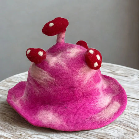 A vibrant shocking pink felted hat with soft marbled texture and three red white spotted mushroom decorations