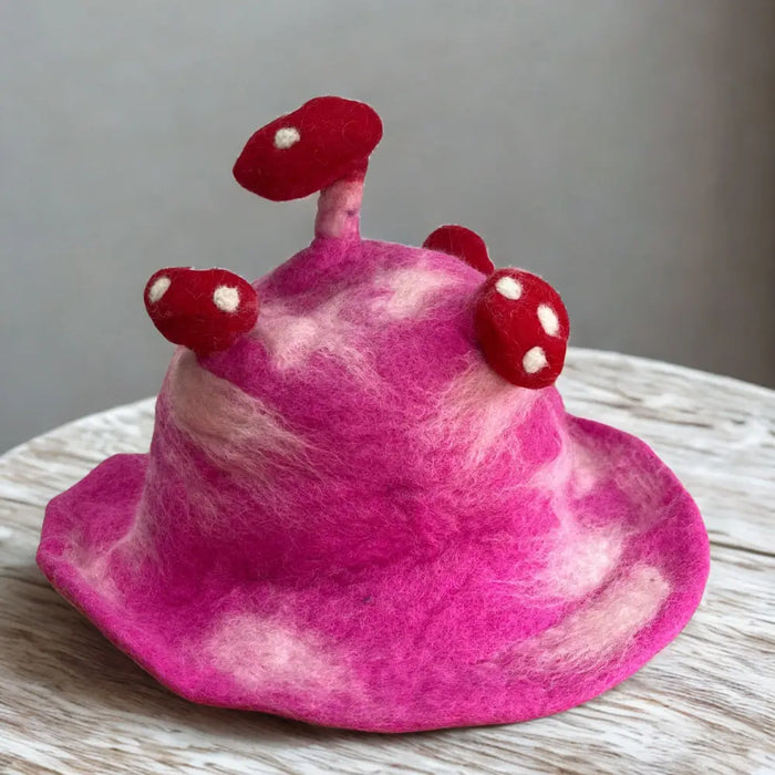 A vibrant shocking pink felted hat with soft marbled texture and three red white spotted mushroom decorations